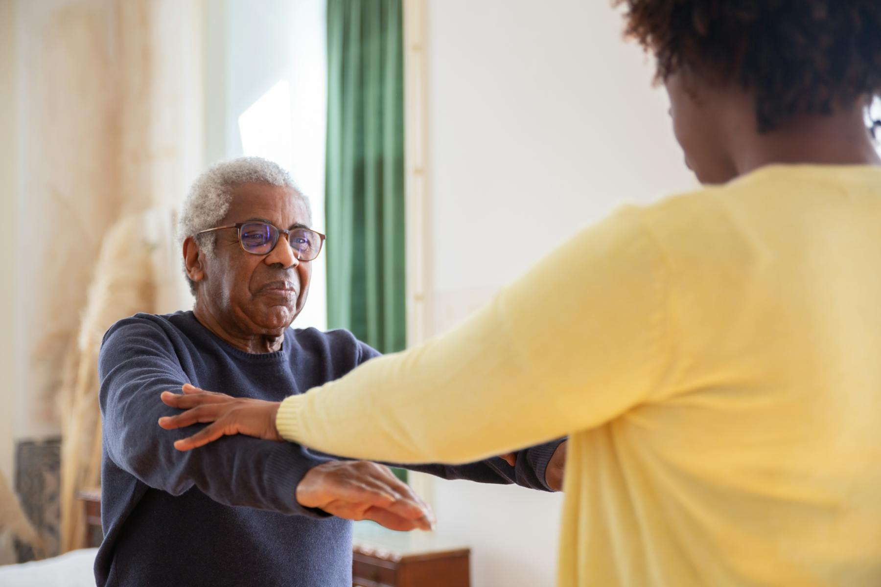 Older adult doing guided therapy exercise at home with a therapist nearby